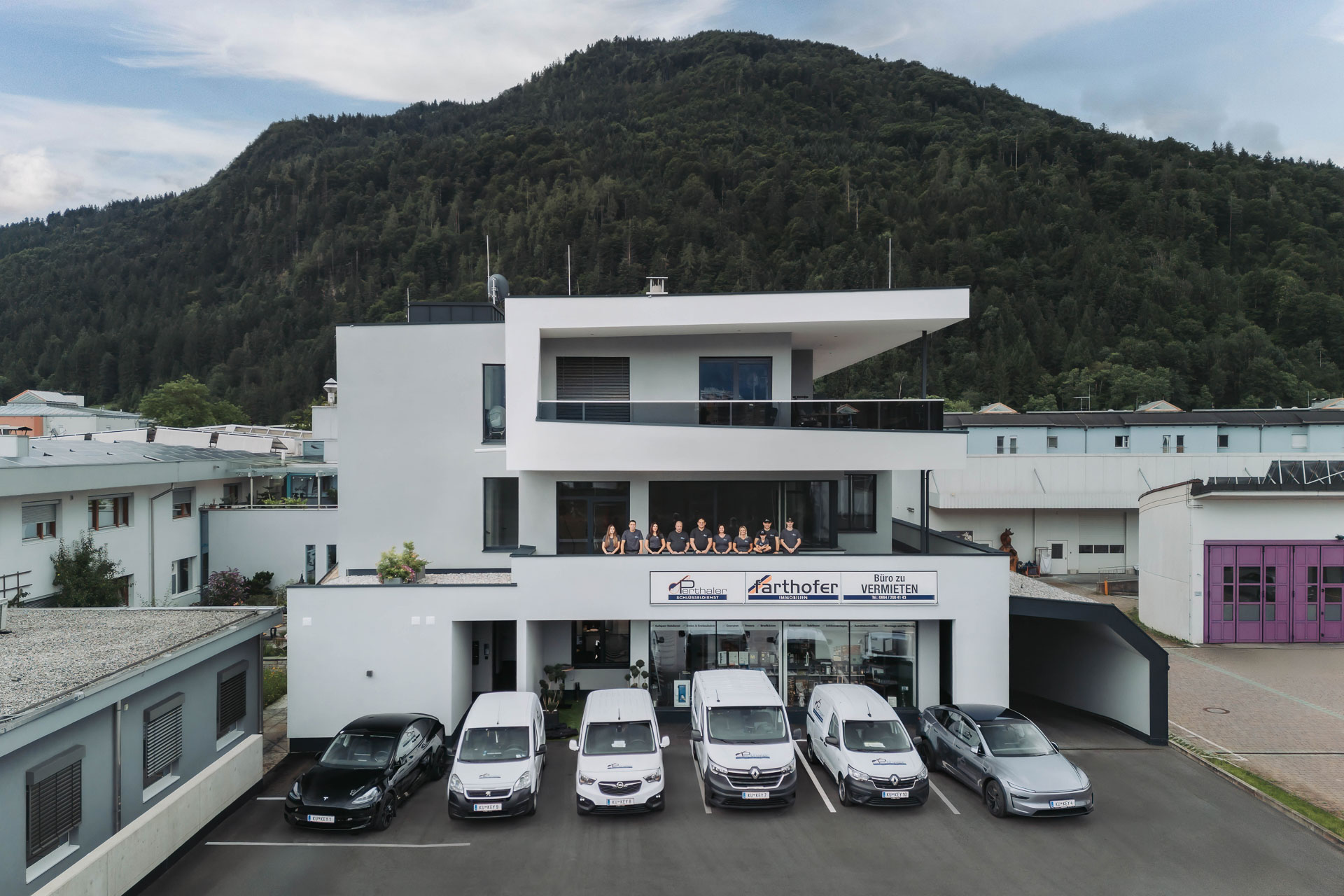 Perthaler GmbH Firmengebäude mit Team und Fahrzeugflotte